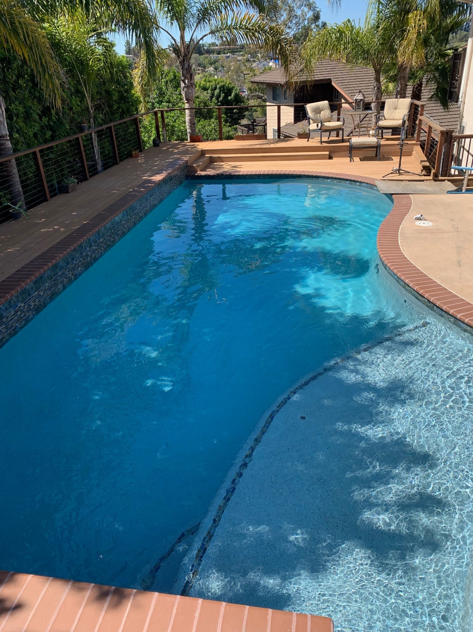 Pool with blue water and tiled edges, surrounded by a deck and trees.