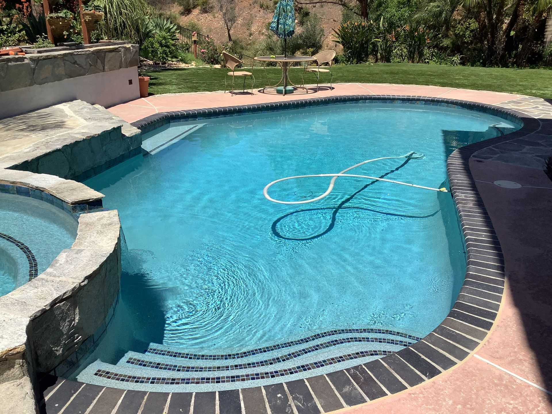 Pool with blue water and surrounding stone deck, steps, and a small hot tub.