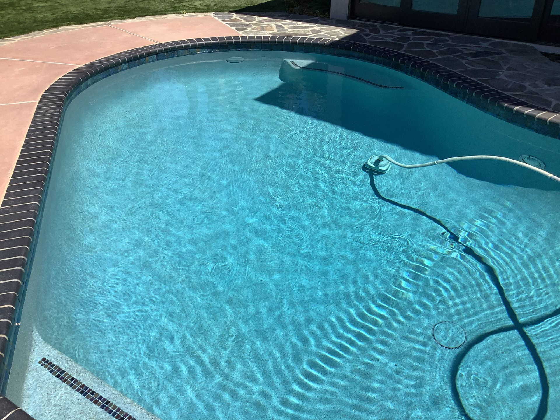 Swimming pool with blue water and a vacuum hose.