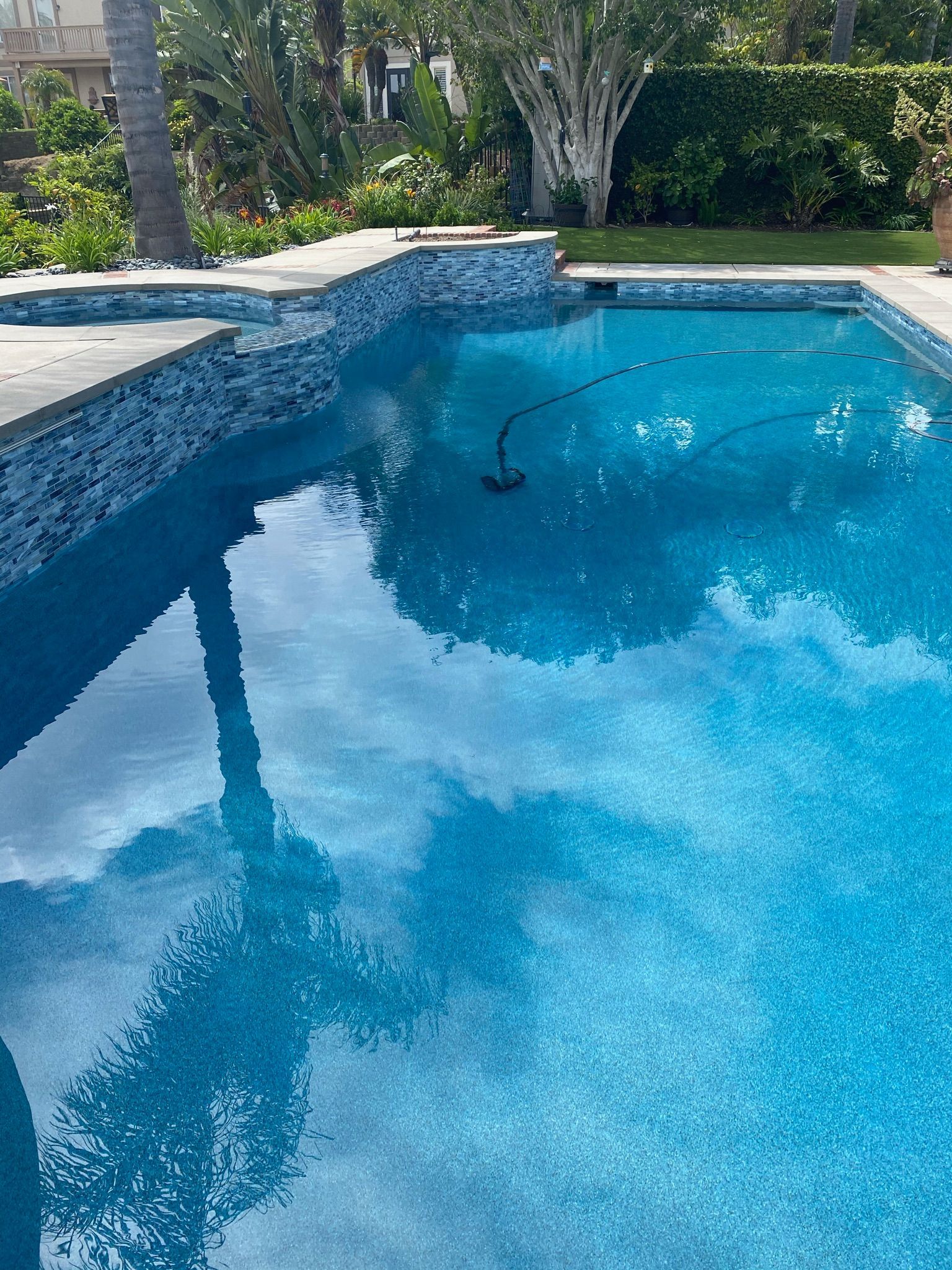 The blue swimming pool reflects the sky and the stone tile border.