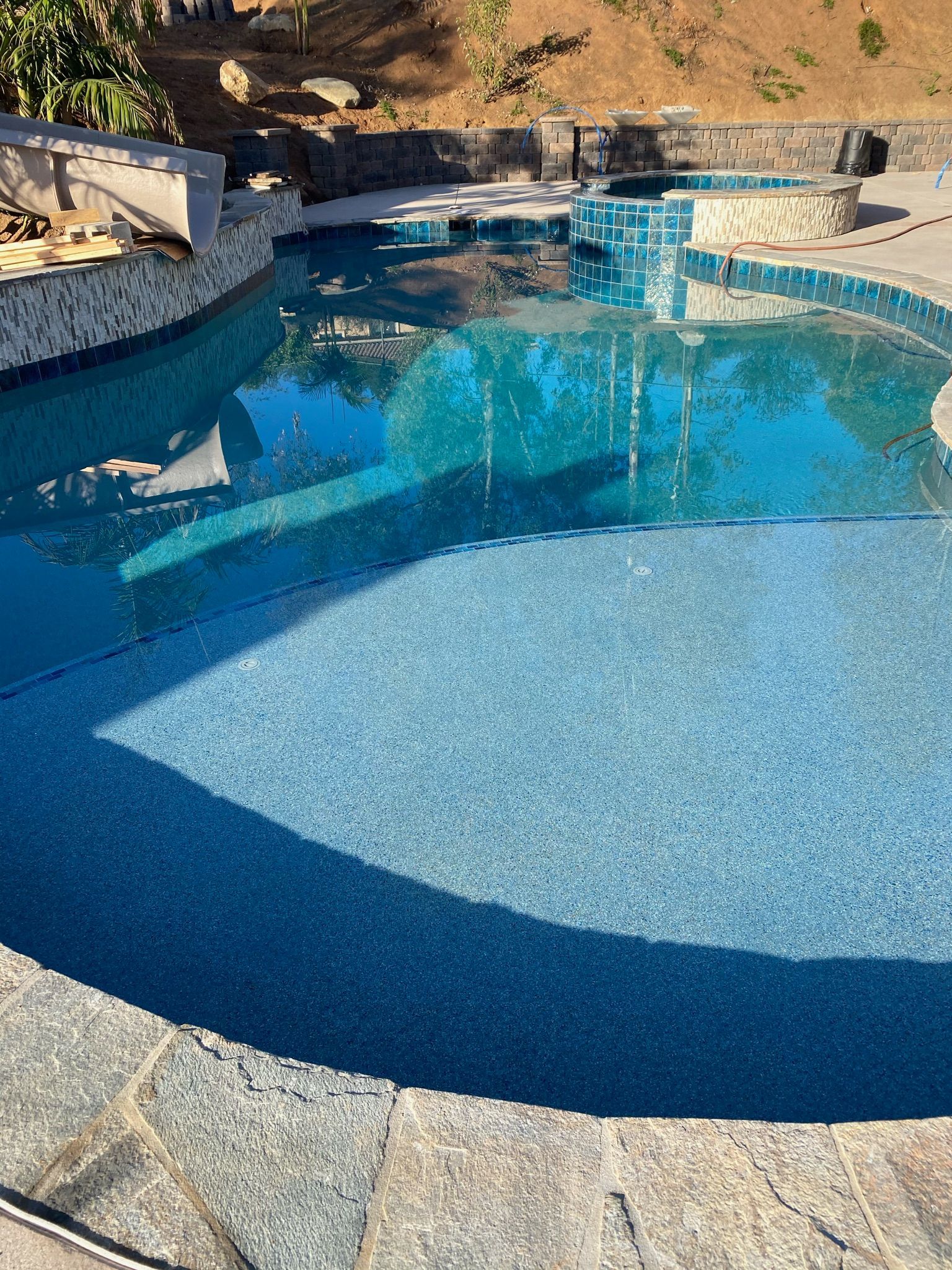 Pool with blue water and stone edging, surrounded by trees and a hillside.
