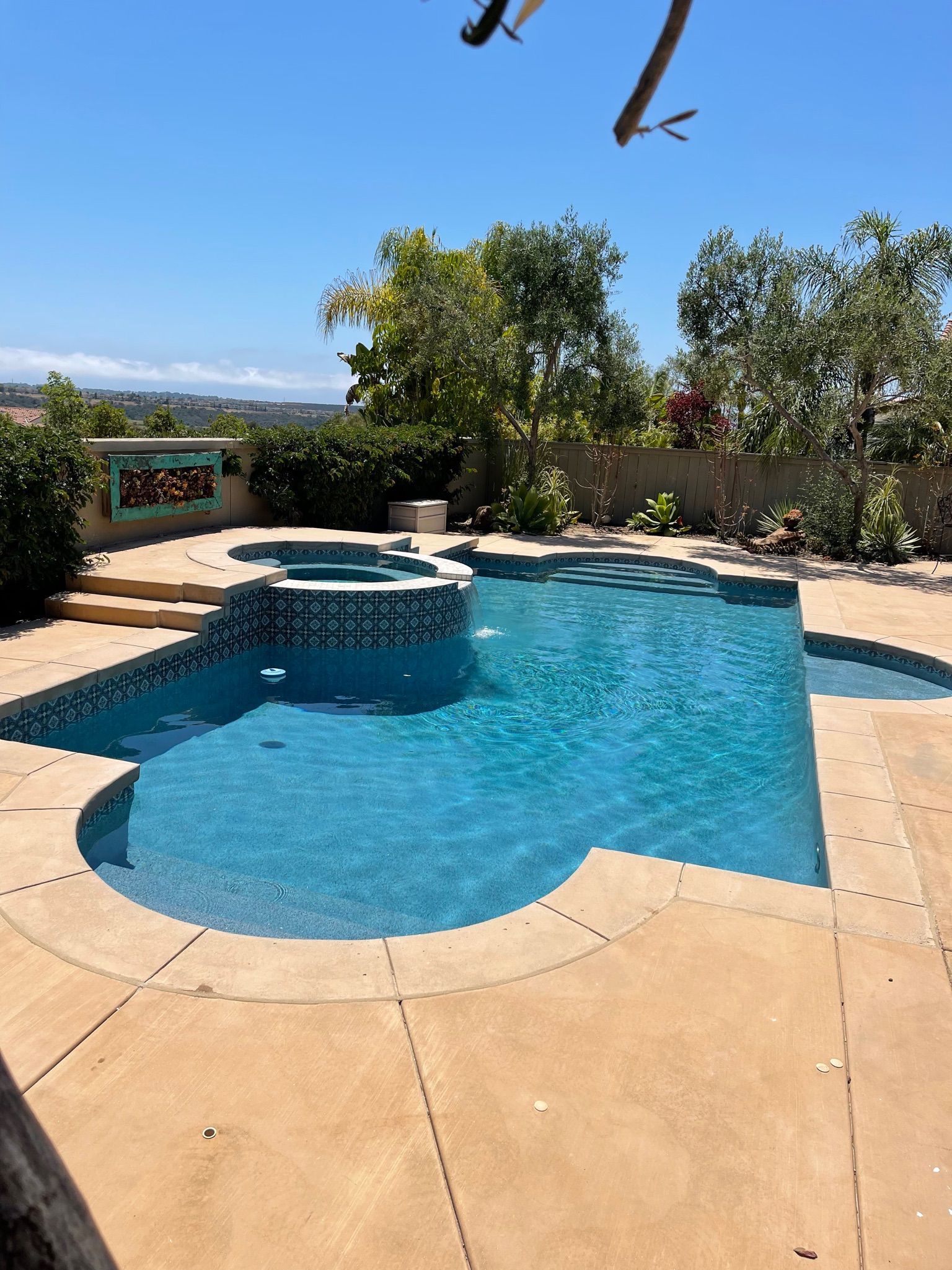 Swimming pool with blue water and a surrounding stone patio on a sunny day.