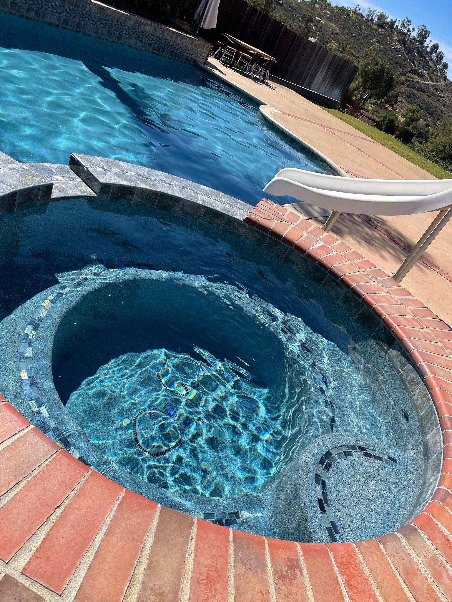 A swimming pool and a hot tub filled with clear, blue water are surrounded by red bricks.