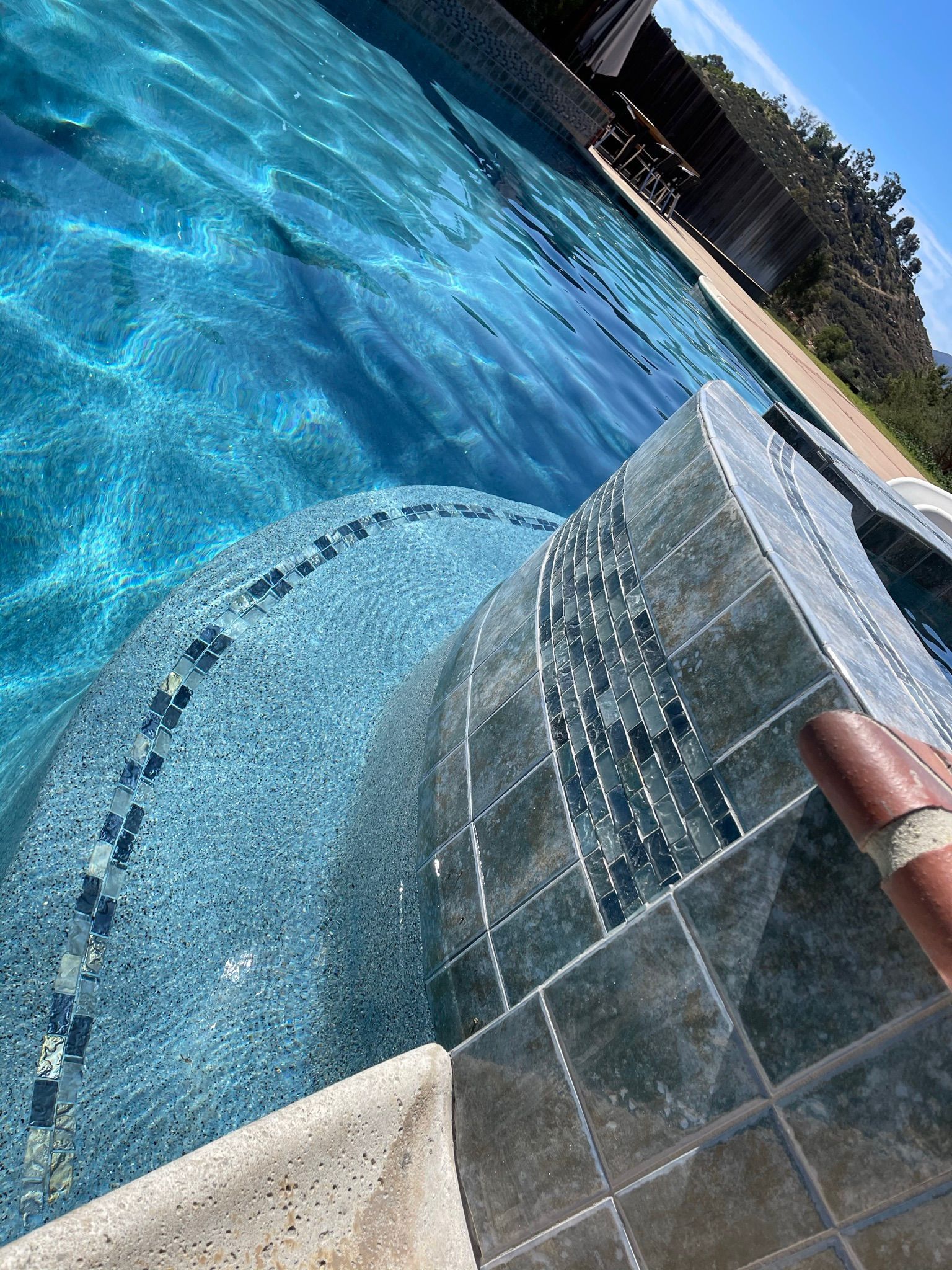 Blue tiled swimming pool with curved wall and sunlight reflecting on the water.