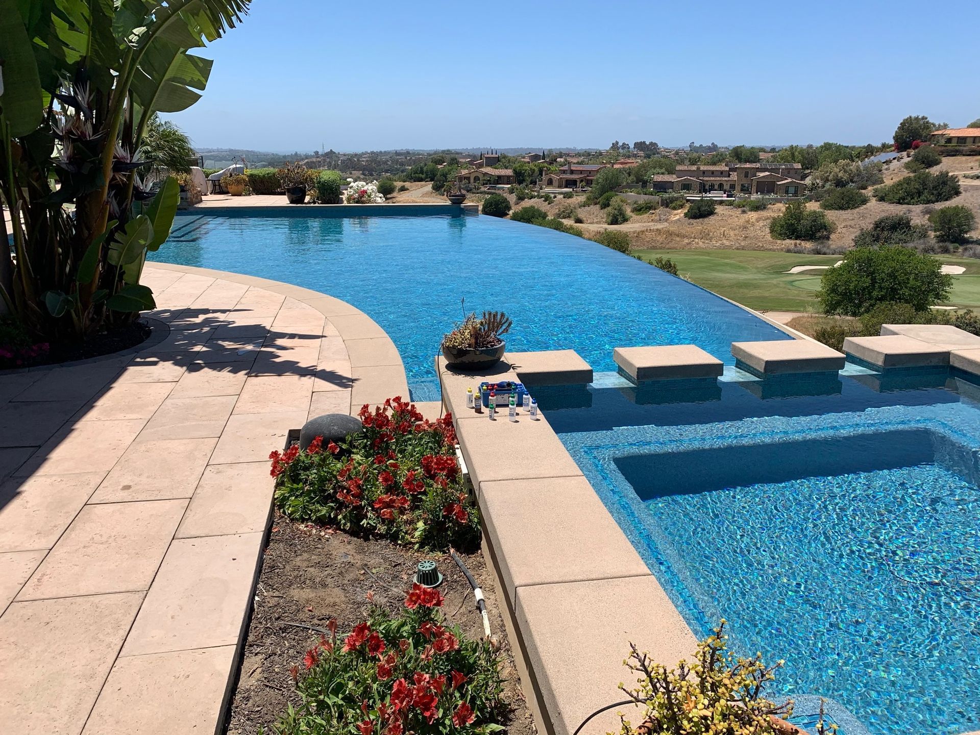Infinity pool overlooking a golf course and distant homes on a sunny day.