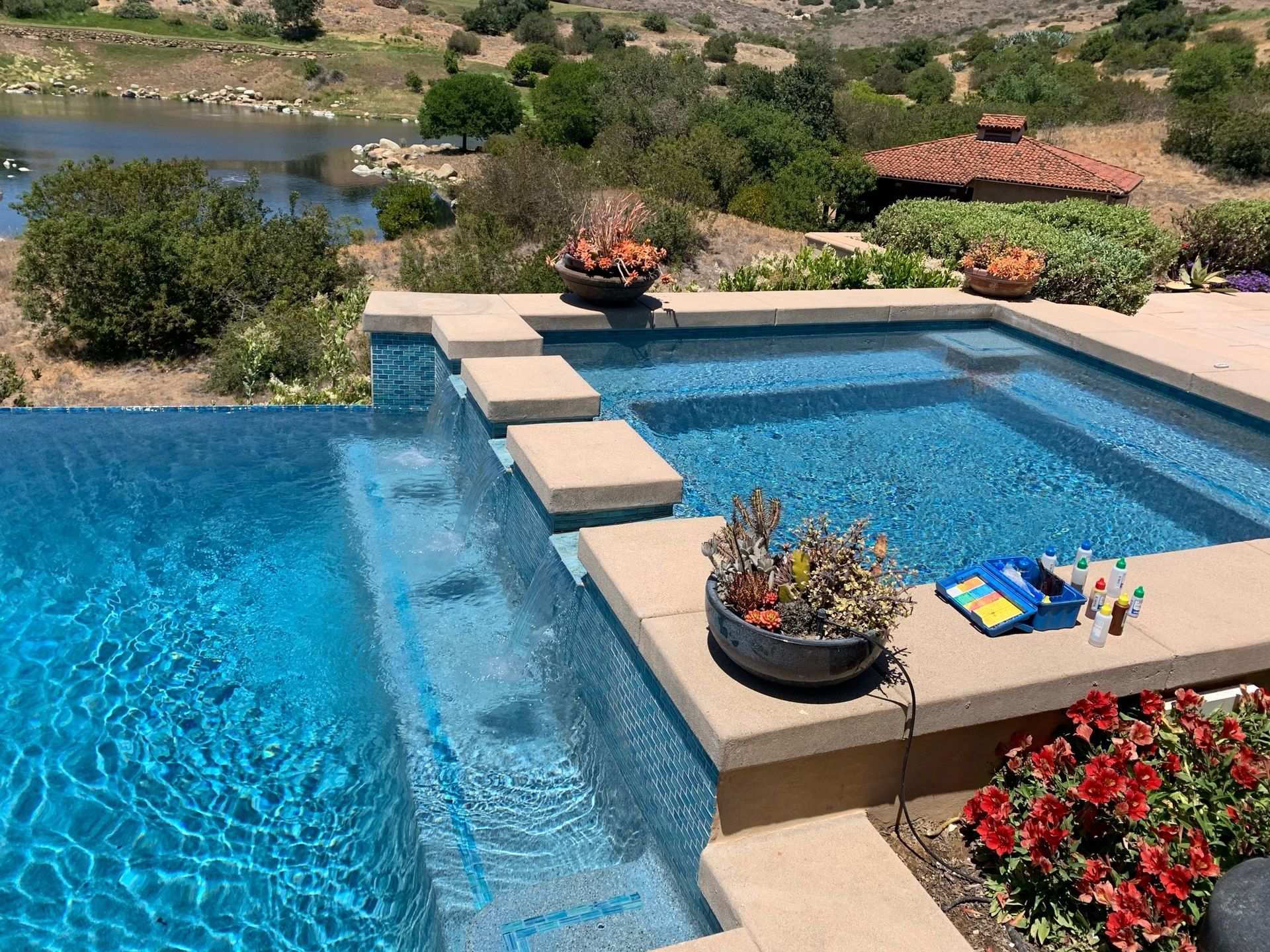 Swimming pool with cascading waterfall, surrounded by stonework, overlooking a lake and hills.