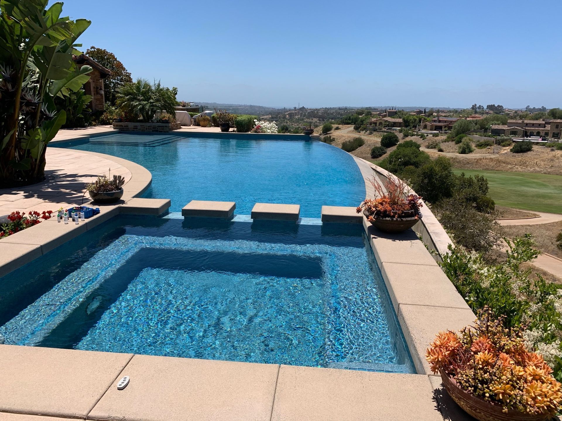 Infinity pool and spa overlooking a golf course and distant hills under a blue sky.