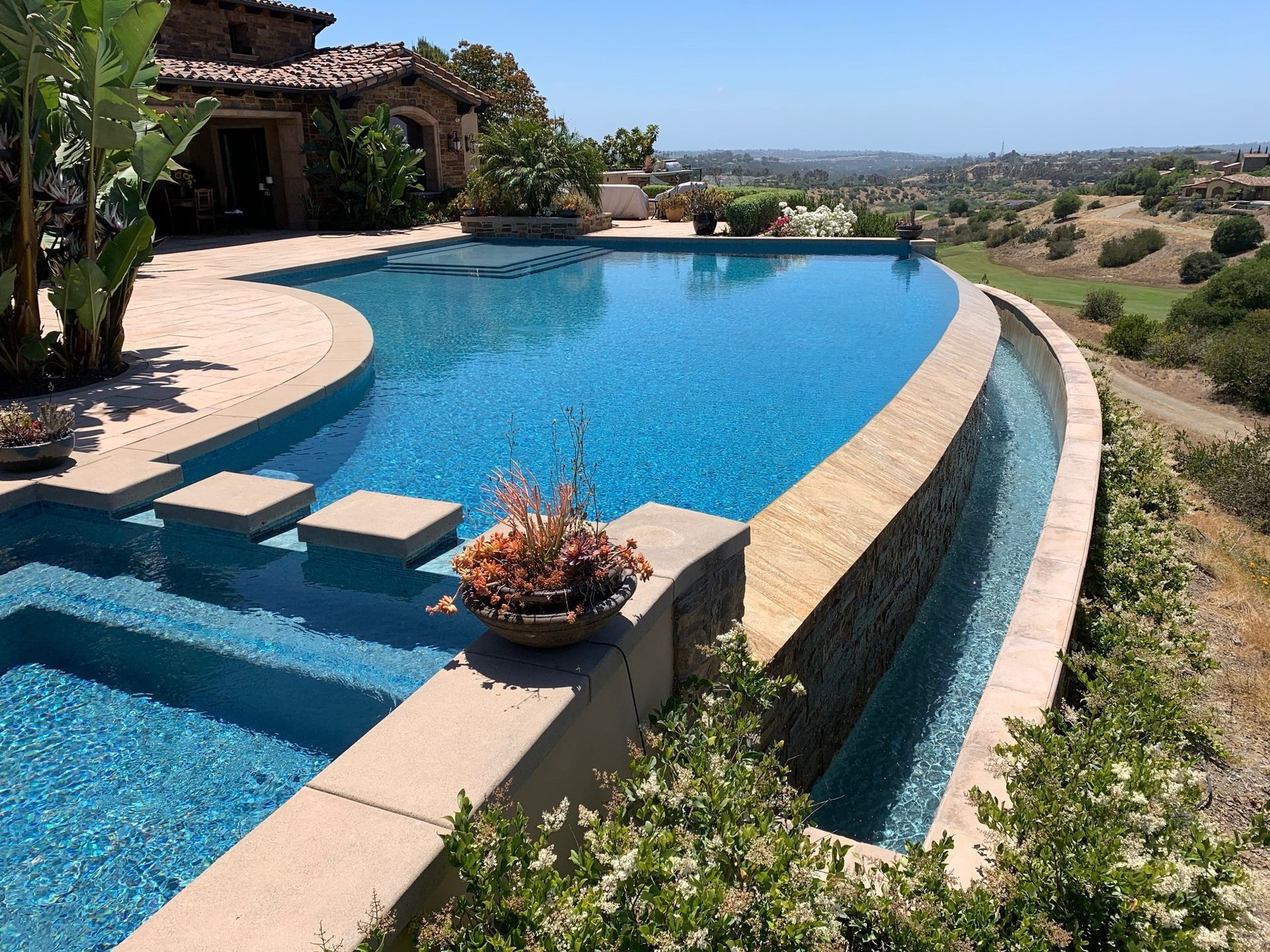 Infinity pool with a waterfall overlooking a scenic landscape on a sunny day.