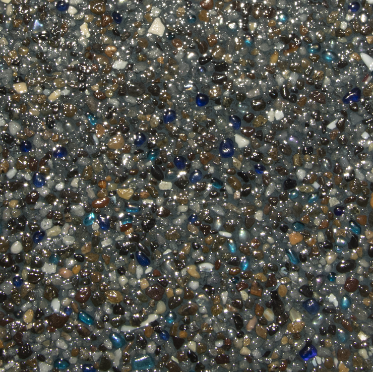 Close-up of a speckled pool finish with various-sized stones and glass beads in shades of gray, blue, and brown.