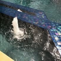 Water fountain in pool with blue tile edging, water spraying up.