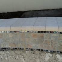 Close-up of a tiled pool edge with mosaic tile band. Light colored coping and aged mortar are visible.