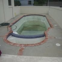 Empty, murky swimming pool with a brick border, viewed from above.