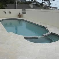 Pool with attached spa, surrounded by light-colored stone patio and white walls.