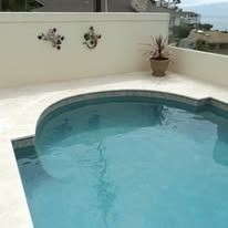Pool with light blue water, surrounded by a beige patio. Two decorative wall sconces and a potted plant are visible.