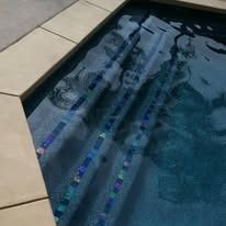Pool steps with dark blue water and light-colored tile border. Steps are lined with colorful mosaic tiles.