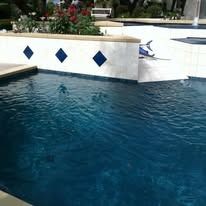 Blue swimming pool with diamond-shaped blue tile border, outdoor setting.
