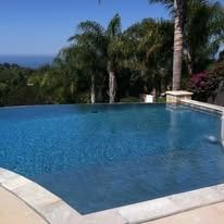 Blue swimming pool with palm trees, sky, and stone border.
