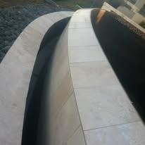 Curved stone wall with rectangular tiles, leading into a shaded area.