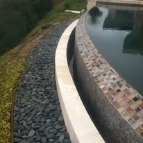 Black river rocks border a curved pool with light-colored coping; green grass on left.