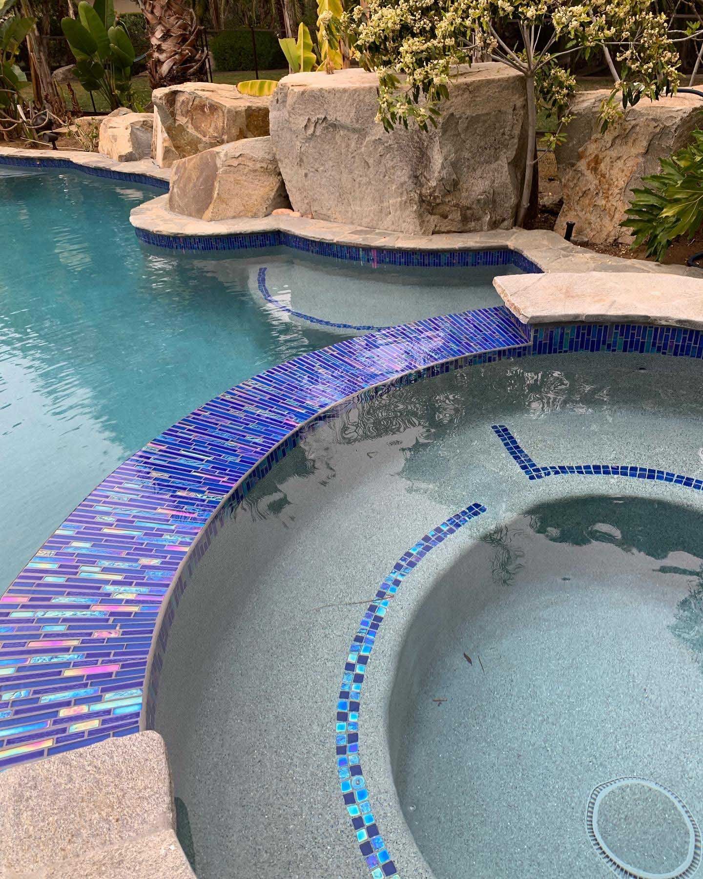 Pool with blue tile border, adjacent spa, and natural stone features. Water is blue.