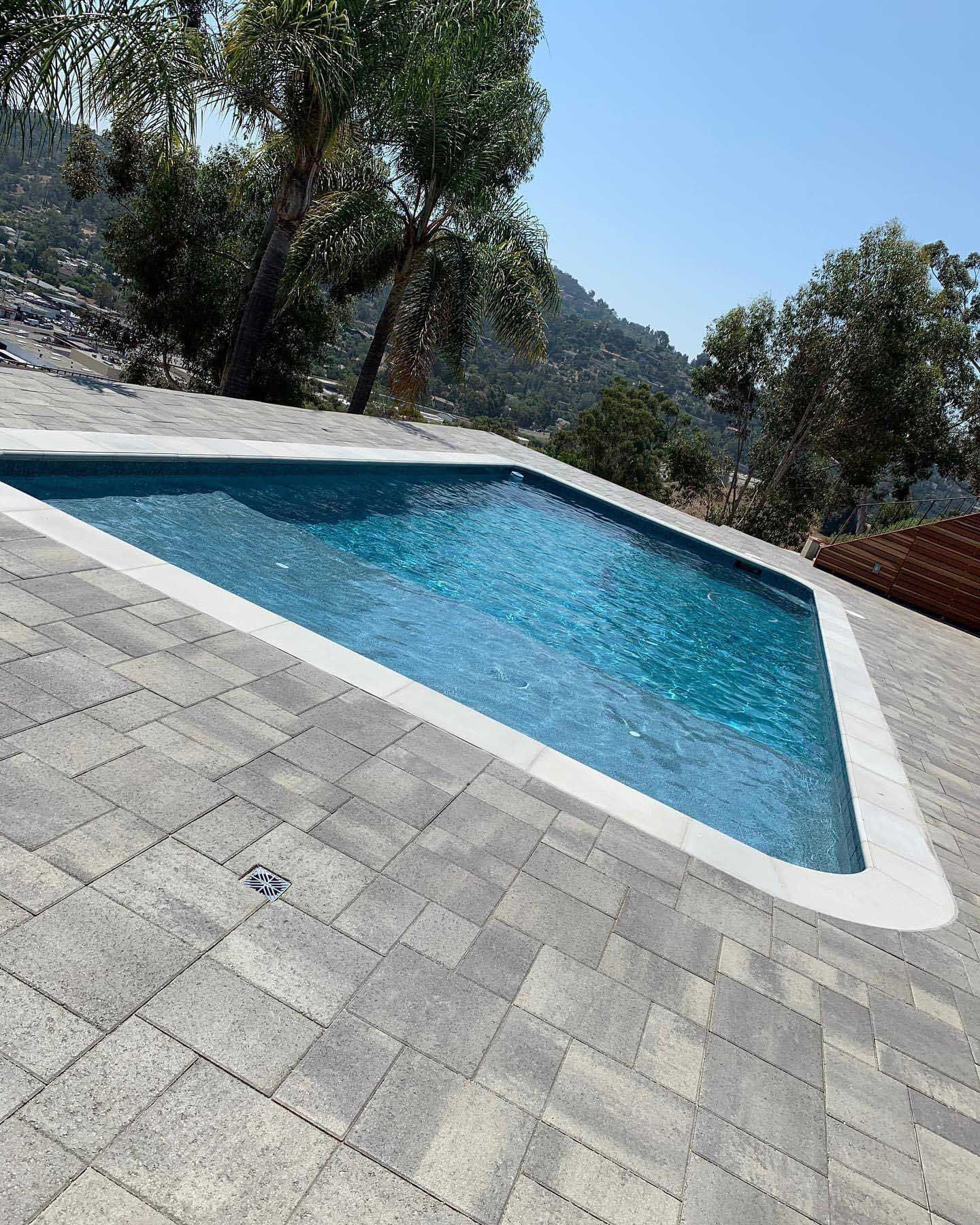 Triangular pool with blue water, surrounded by gray paving stones, set against a mountain backdrop.