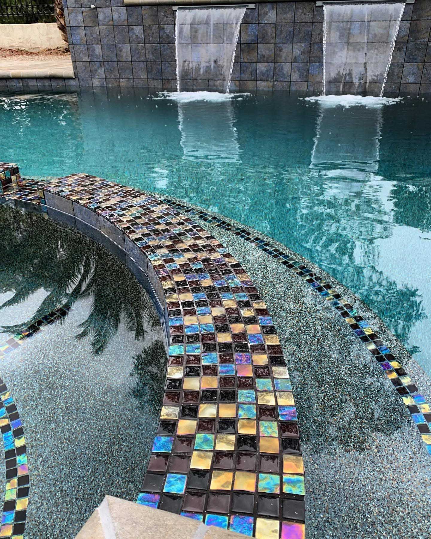 Pool with iridescent tile border, waterfall feature, and turquoise water.