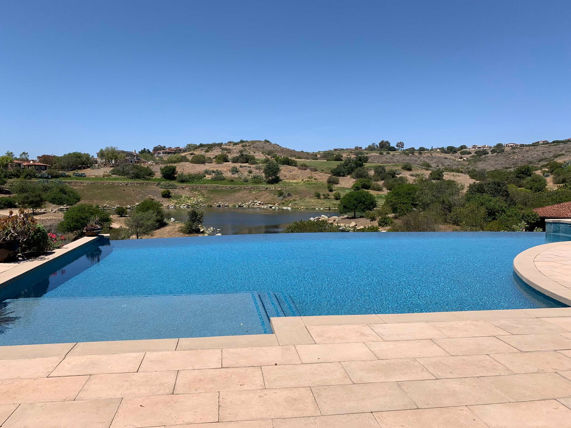 Infinity pool with blue water overlooking a lake and hills under a clear sky.