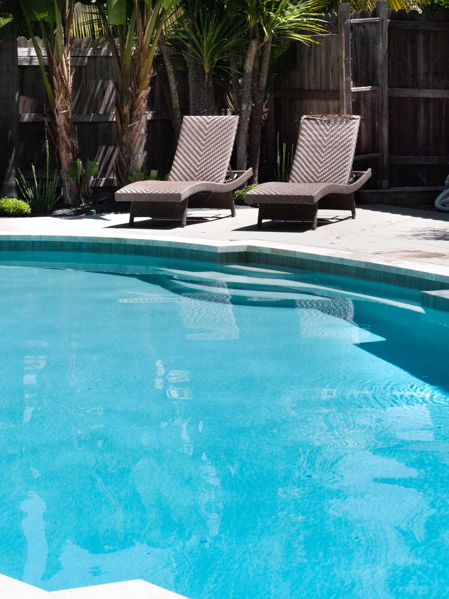 Two lounge chairs on a patio beside a turquoise swimming pool.