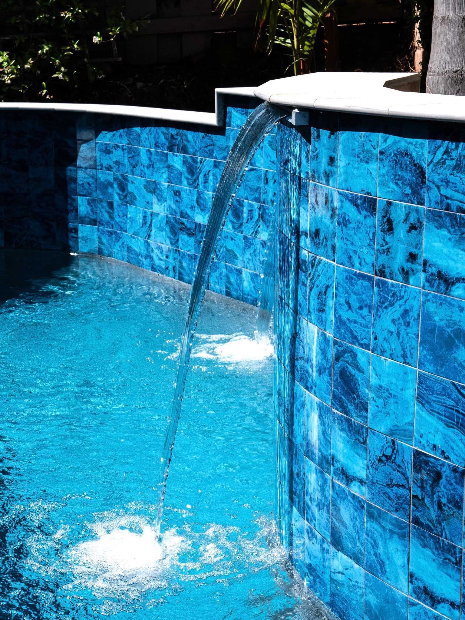 Blue-tiled pool with a waterfall feature. Water cascades down from the edge into the pool.