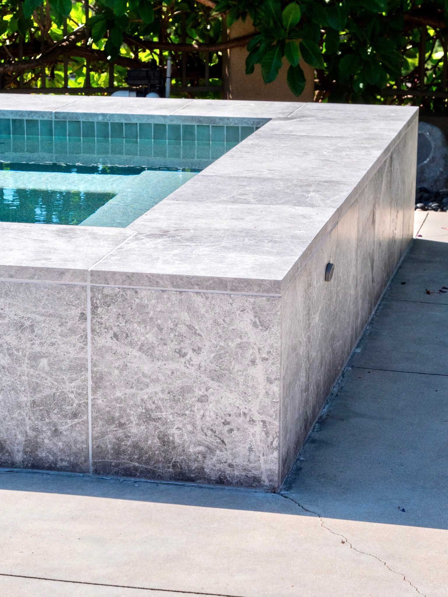 Pool edge made of gray stone with turquoise water and concrete patio.
