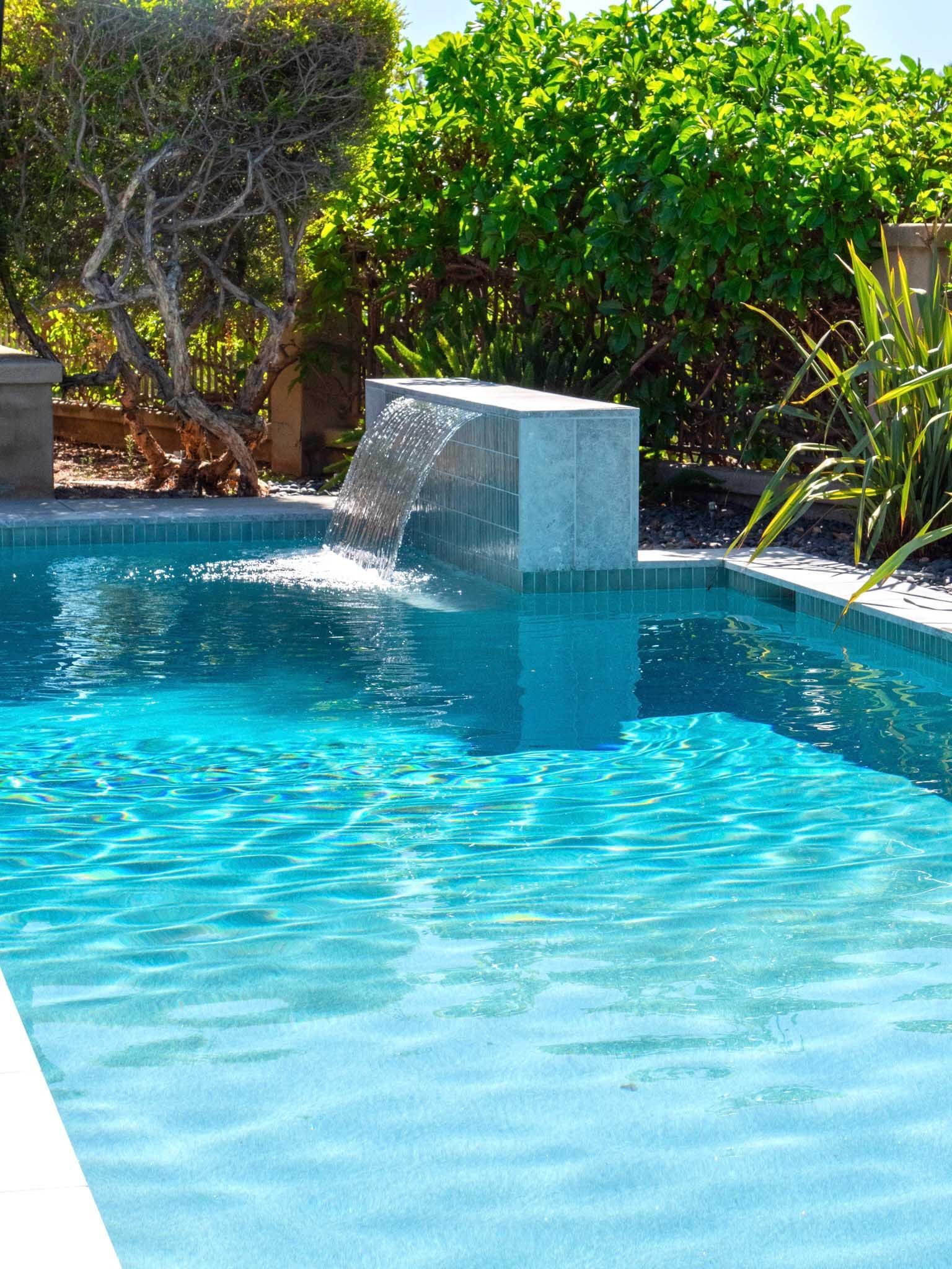 Swimming pool with a water feature, turquoise water, and lush greenery.