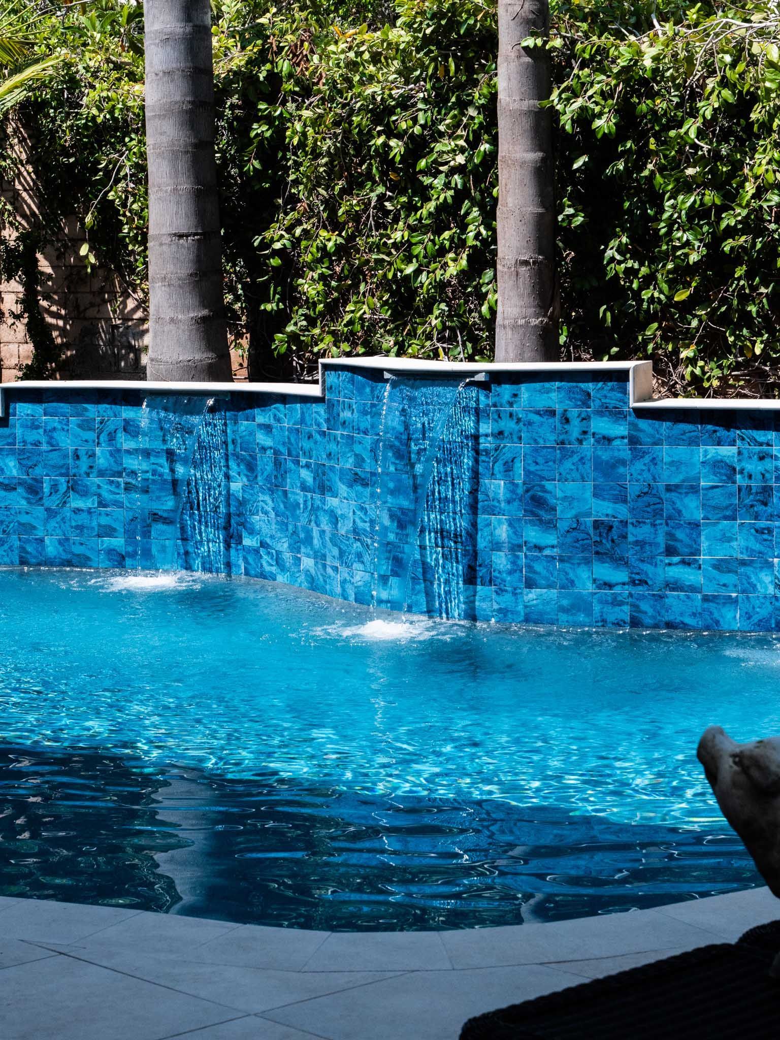Blue tiled waterfall cascading into a pool. Palm trees and greenery in the background.