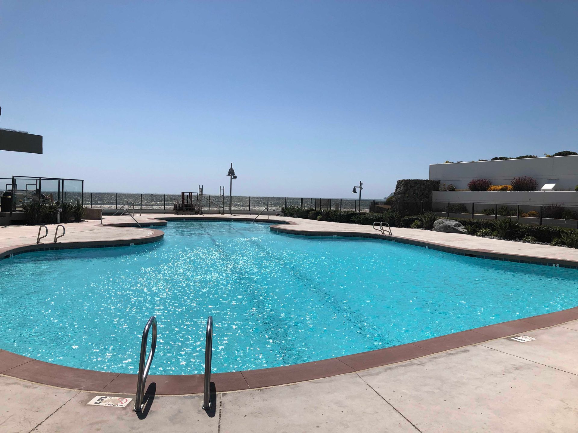 A sparkling blue pool with ladder, overlooking the ocean under a clear sky.