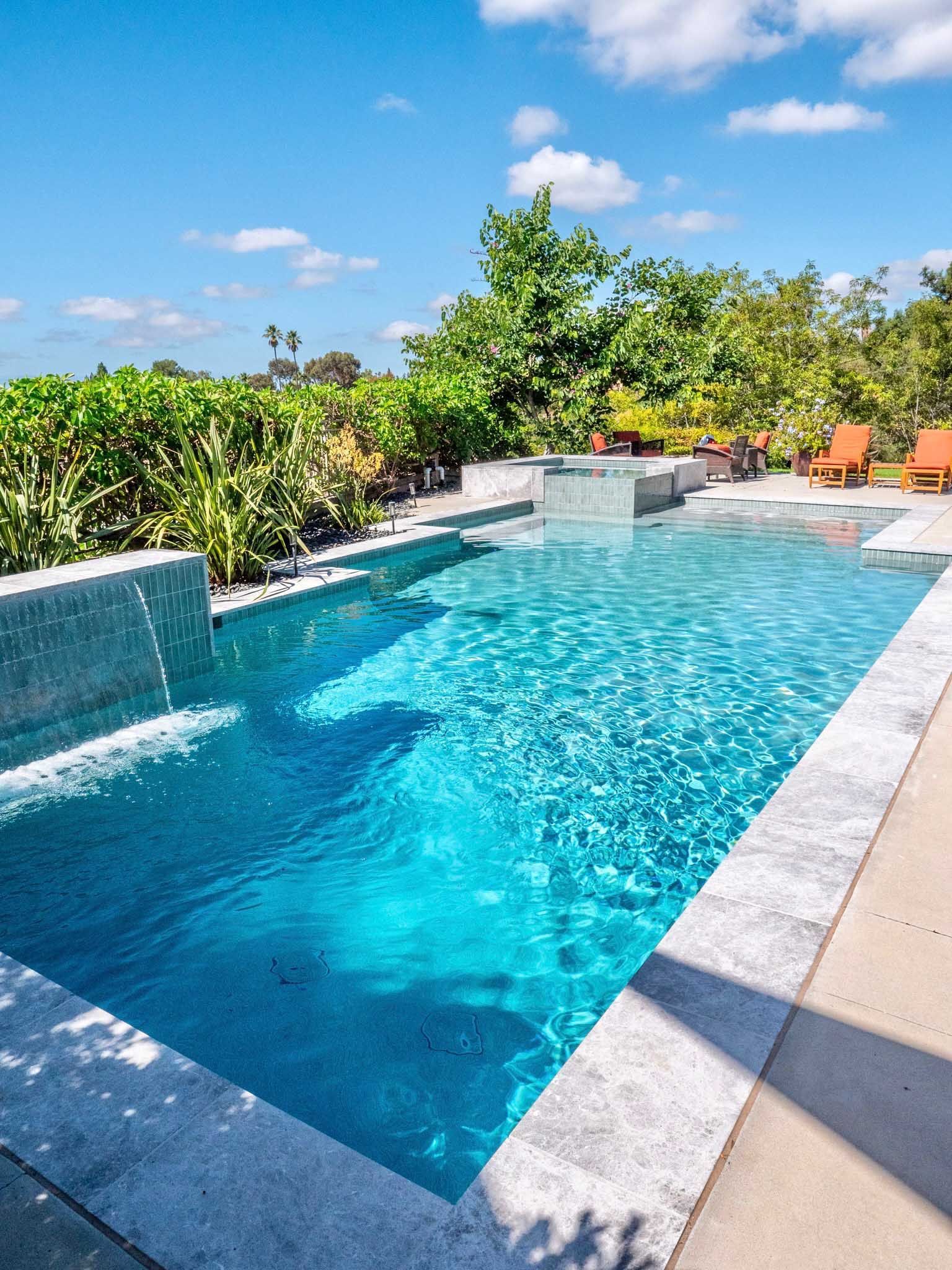 Swimming pool with turquoise water, waterfall features, and surrounding greenery under a blue sky.