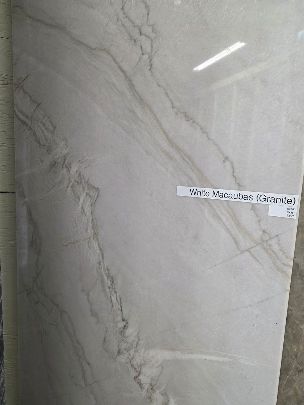 A light-colored, polished floor tile with thin, grey marble-style veining and a small label attached to the center.