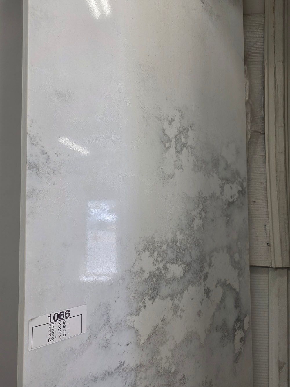 A tall, vertical slab of polished white quartz countertop with light grey, marble-like veining.