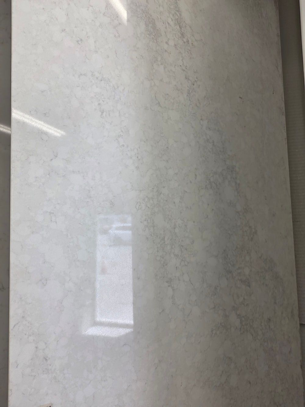 A single, polished, light-gray marble or stone tile with faint, wispy white and grey veining throughout.