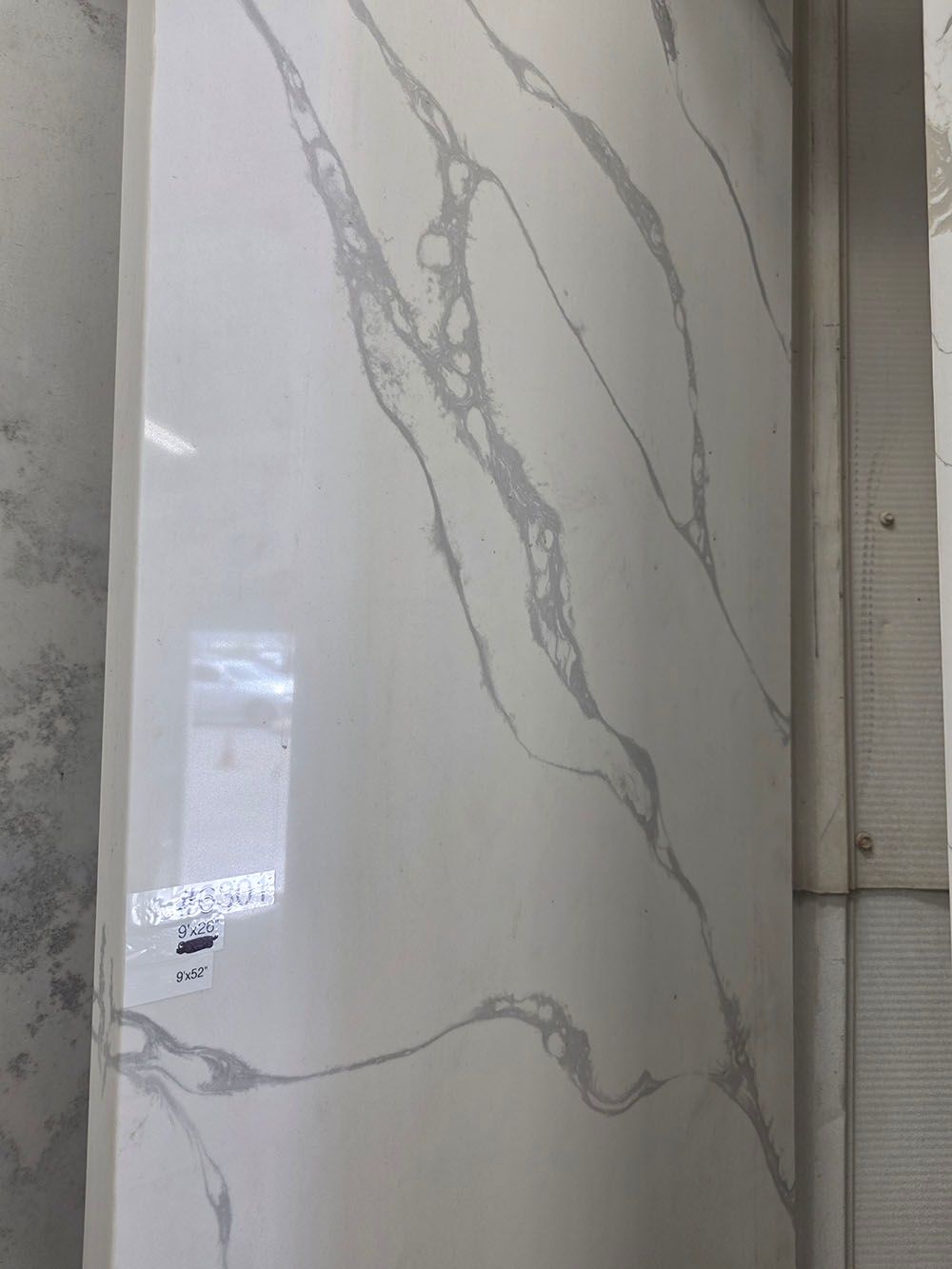 A vertical, polished quartz slab with a white base featuring bold, flowing grey marble veining.
