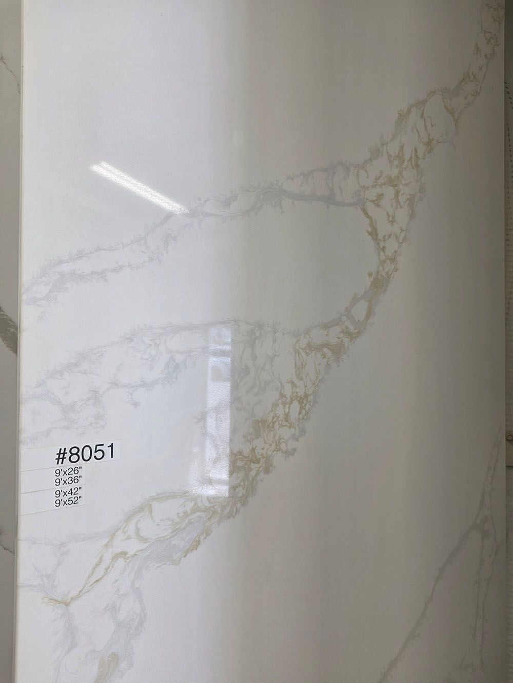 A glossy, white quartz slab featuring prominent, organic light brown and grey veining.
