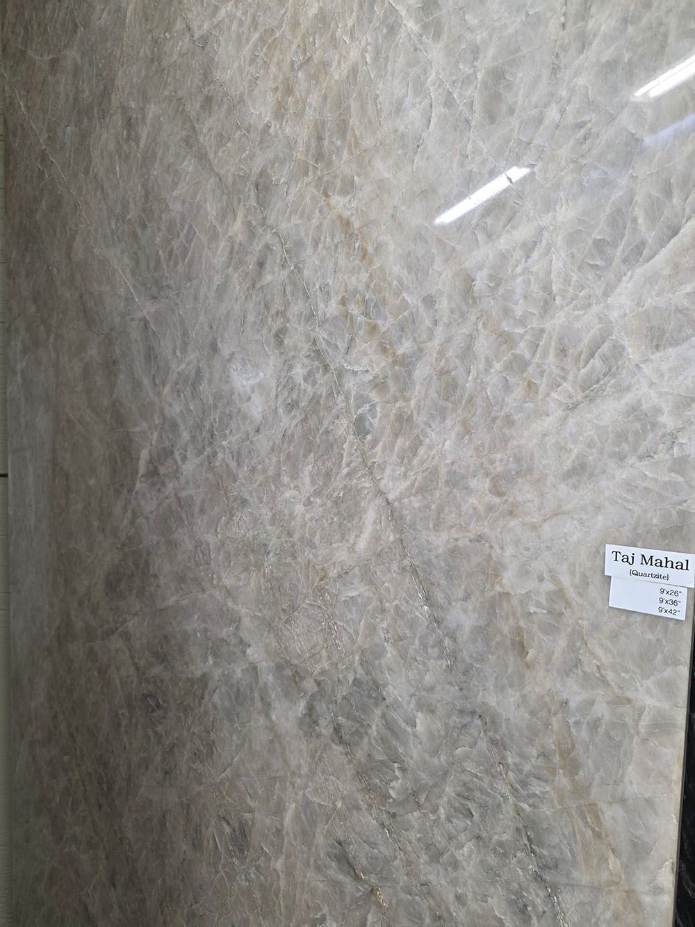 A large slab of polished, light grey and beige marble with intricate, cracked white veining throughout.