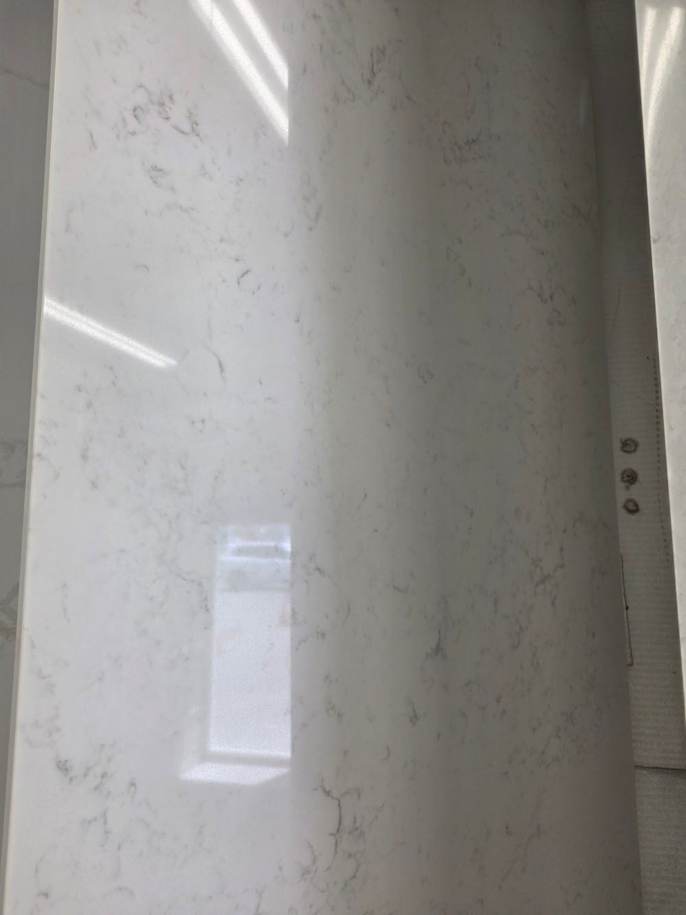 A polished slab of white quartz countertop with light grey veining, shown in a brightly lit indoor showroom.