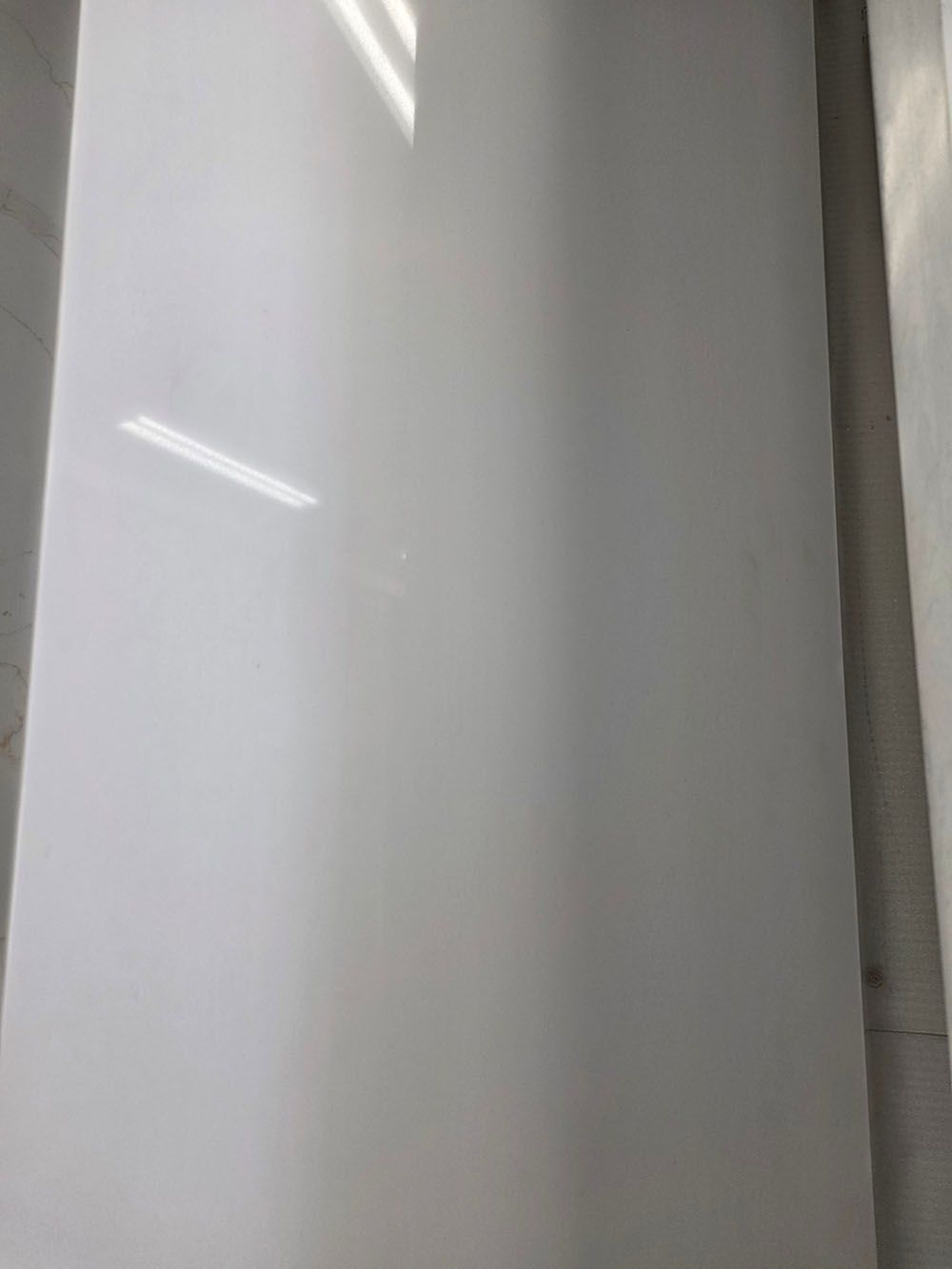 A vertical, glossy white surface with subtle reflections from overhead lighting.