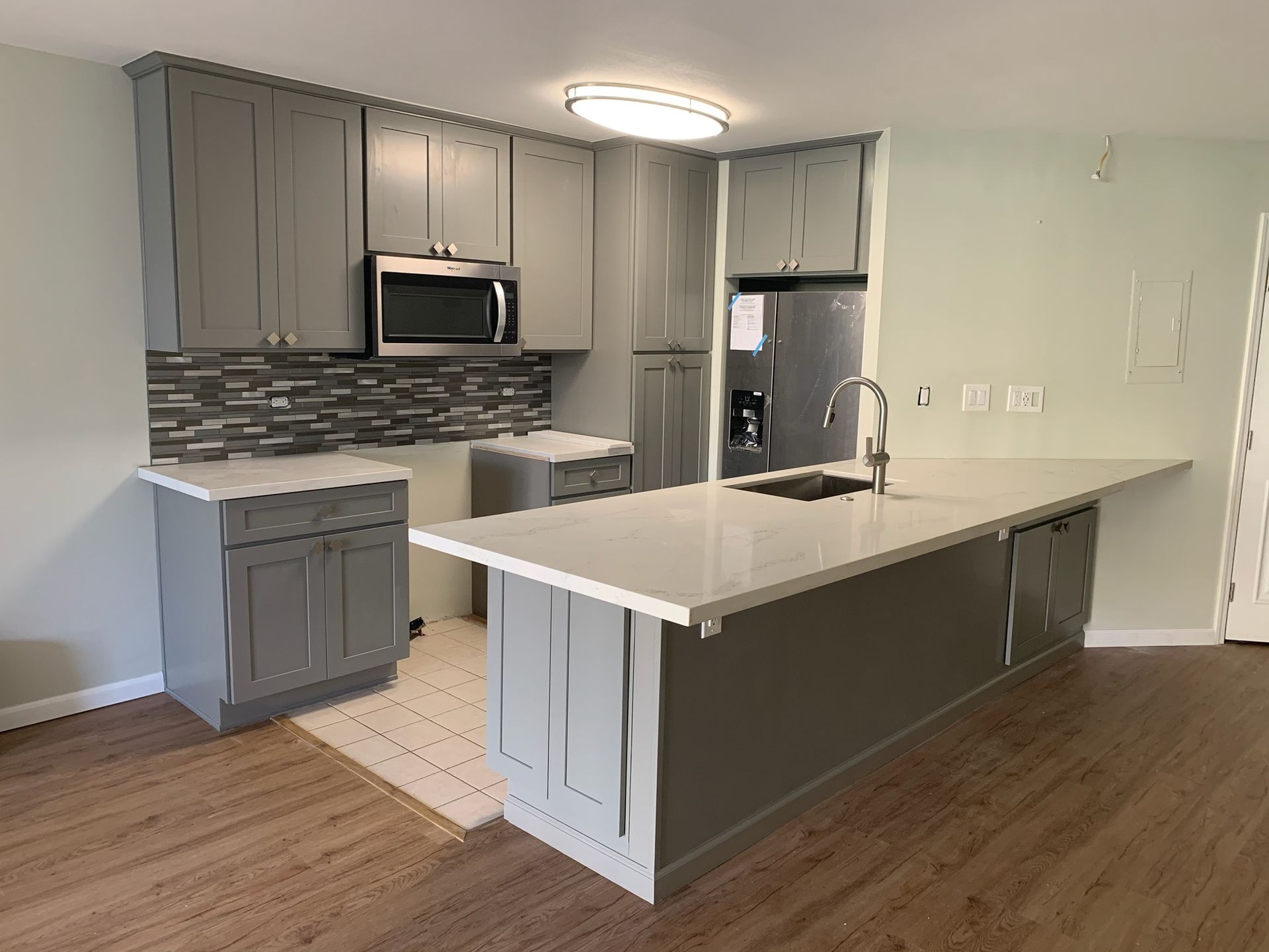 A kitchen with gray cabinets and white countertops.