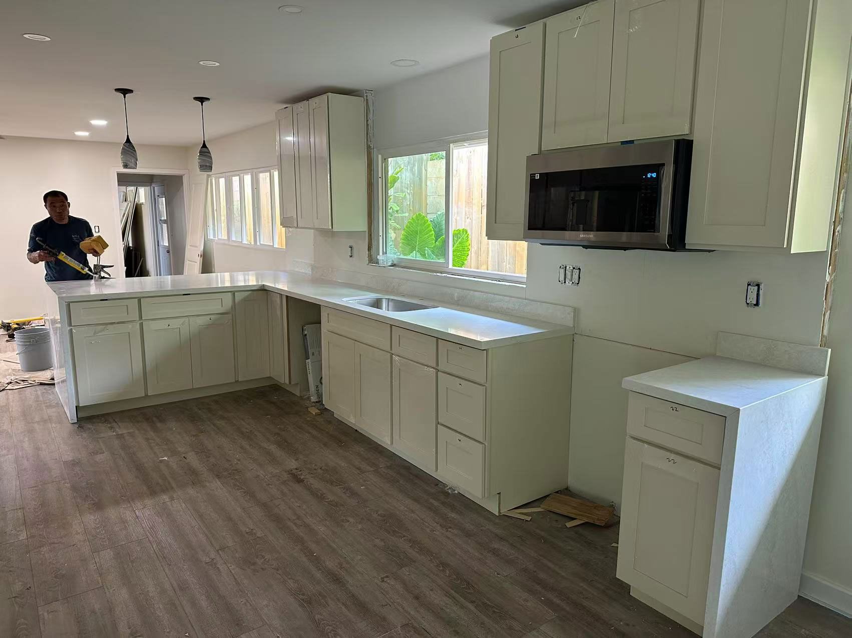 A man is standing in a kitchen with white cabinets and stainless steel appliances.