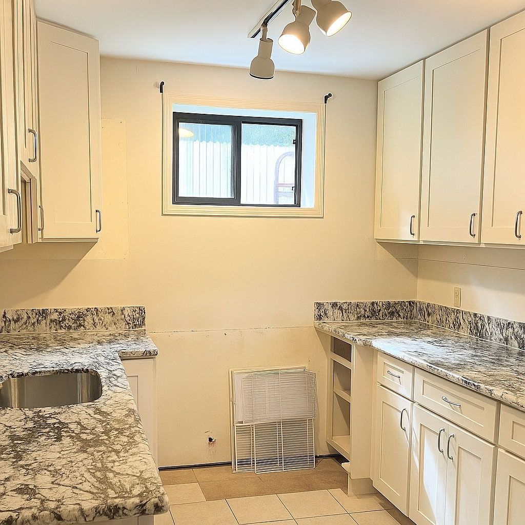 A kitchen with white cabinets, granite counter tops, a sink, and a window.