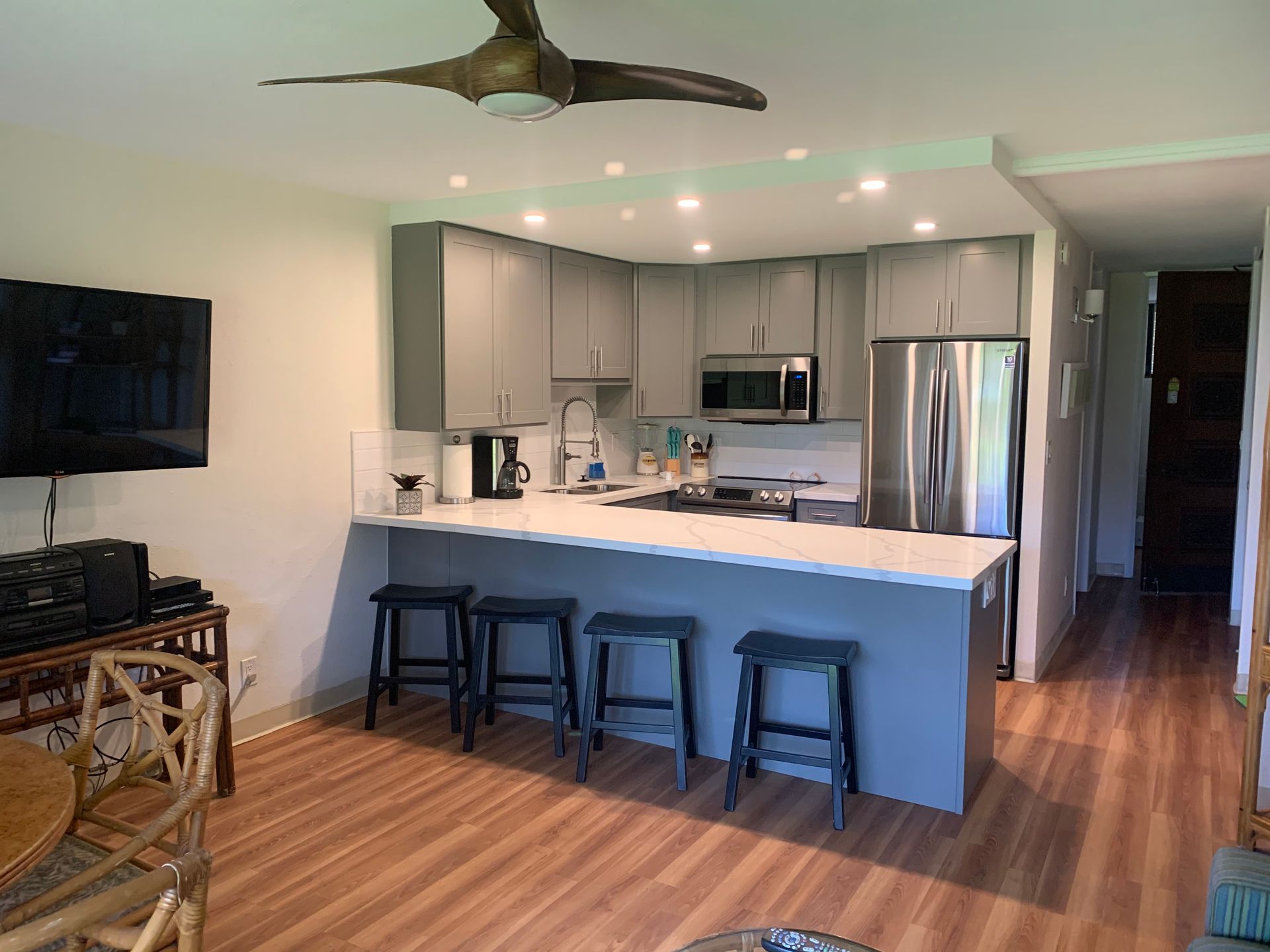 A kitchen with stools and a ceiling fan in a living room.