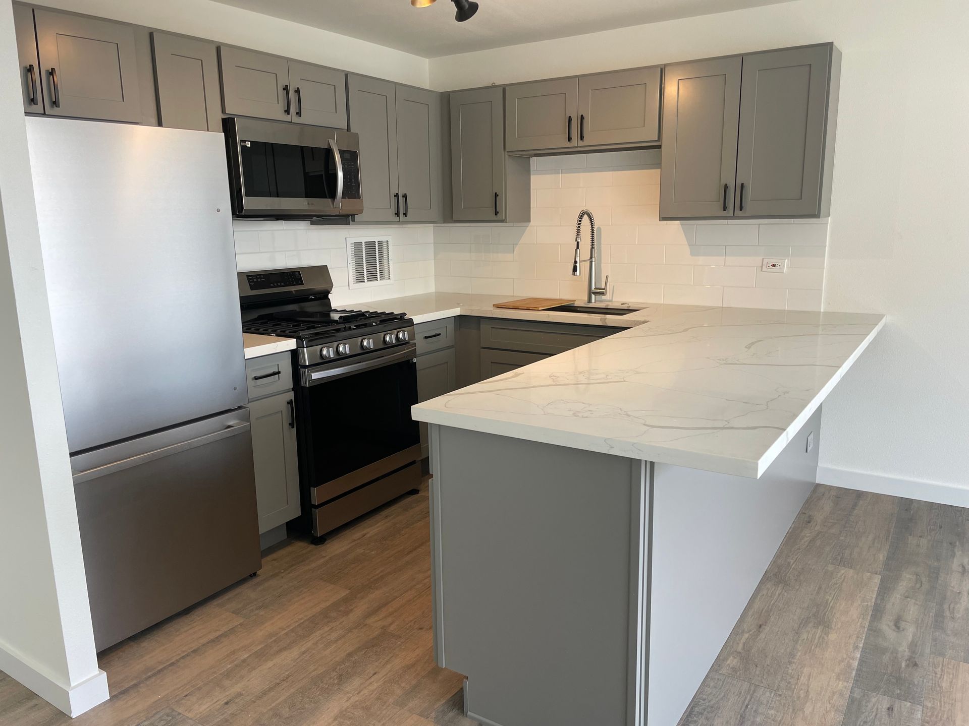 A kitchen with stainless steel appliances and gray cabinets.