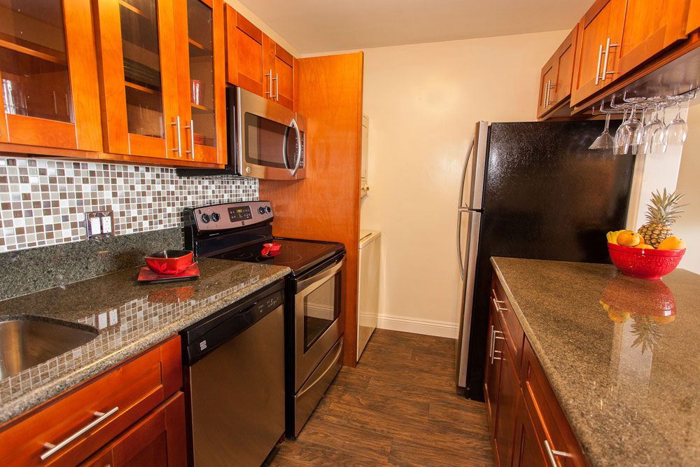 A kitchen with stainless steel appliances, granite counter tops, wooden cabinets, and a black refrigerator.