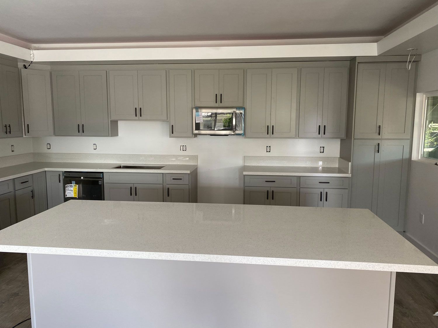 A kitchen with gray cabinets and white counter tops and a large island.