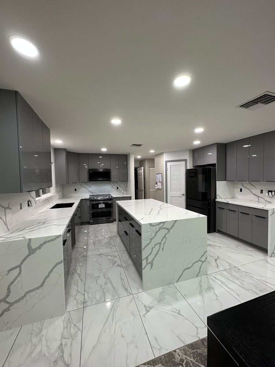 A kitchen with marble counter tops, gray cabinets, and a large island.